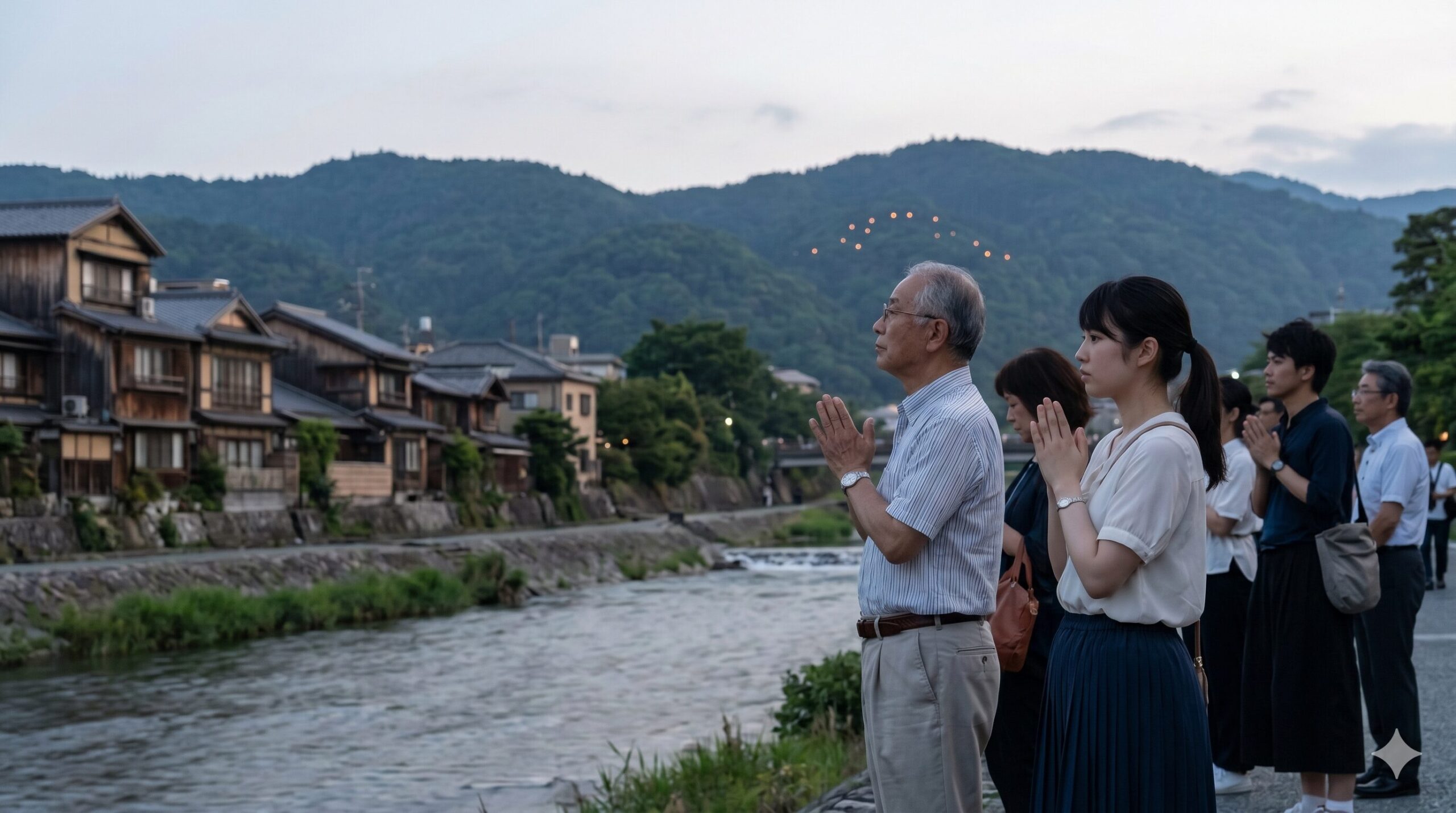 夏の夕暮れ、京都の鴨川沿いで遠くの山を静かに見つめ、祈りを捧げる日本人のグループ。