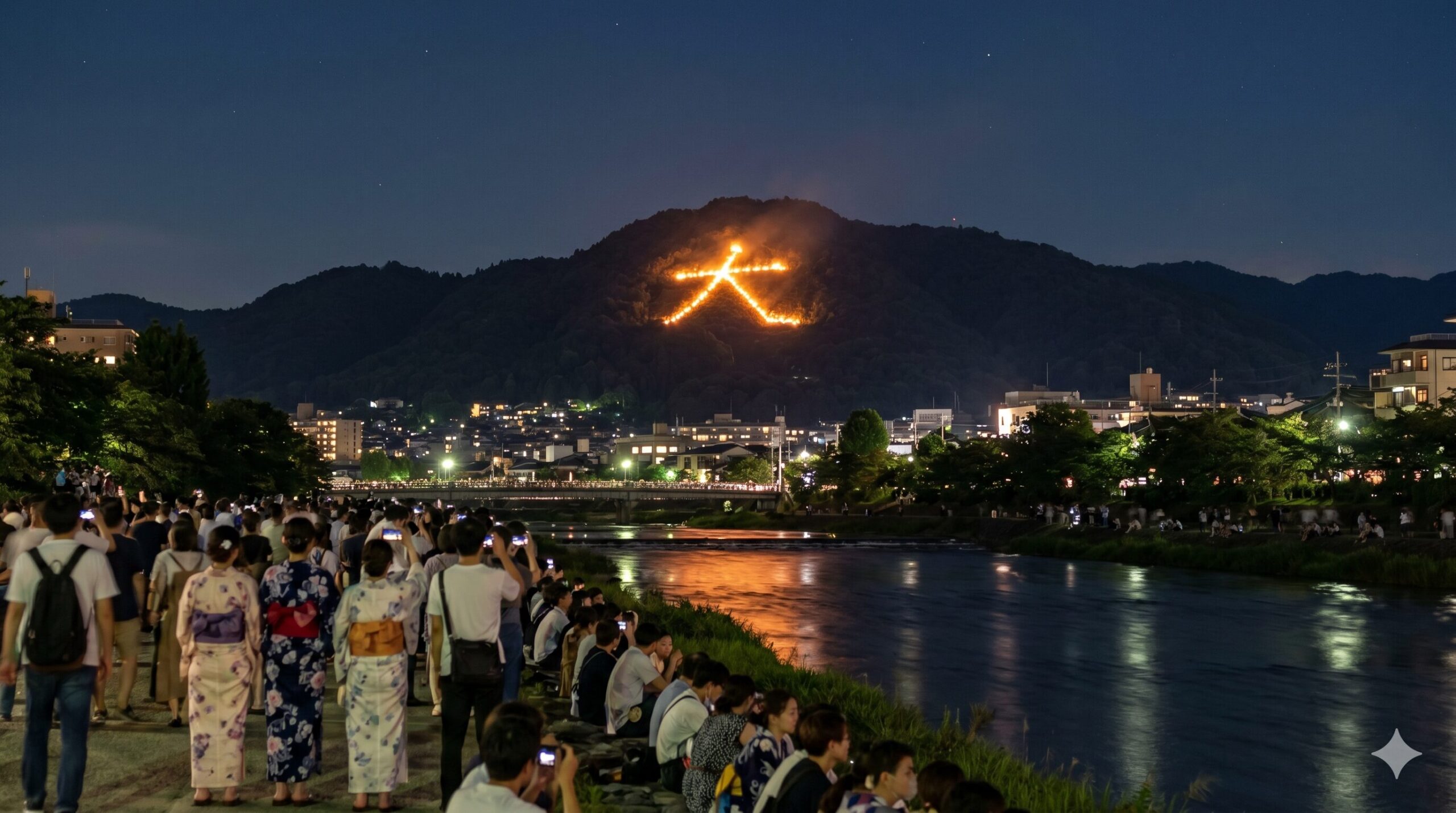 京都の鴨川沿いから眺める、夜空に明るく浮かび上がる五山送り火の「大文字」。