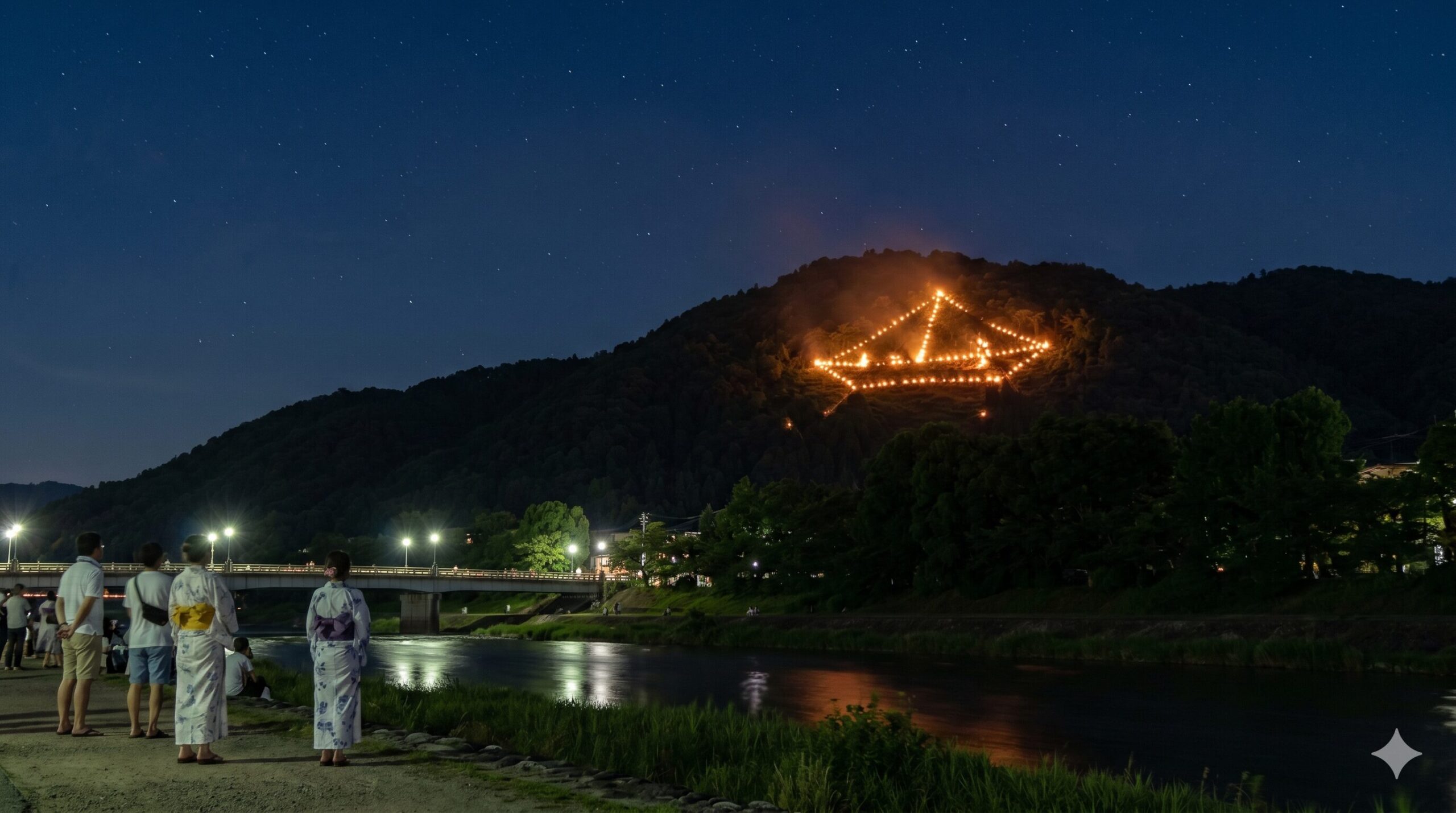 京都の賀茂川西岸から見上げる、山肌に鮮やかに灯る「船形万灯籠」の送り火。