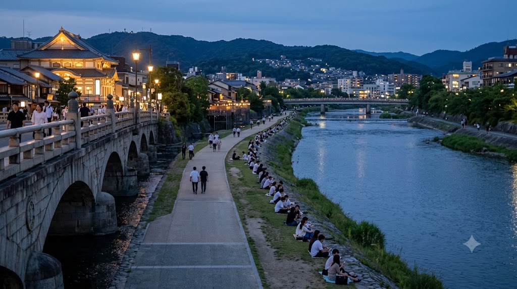 夕暮れ時の京都・鴨川、三条・四条大橋間の右岸河川敷。日本人カップルやグループが川を向いて等間隔に座り、景色を楽しんでいる。