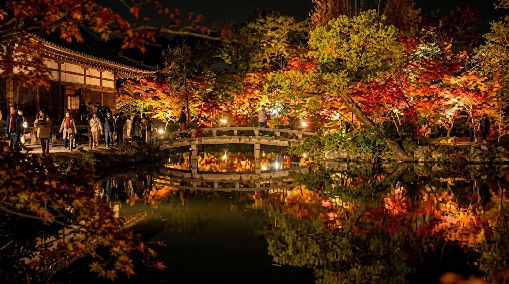 夜の帳が下りた京都の寺院で、ライトアップされた鮮やかな紅葉と石橋が、放生池の水面に鏡のように美しく反射する幻想的な光景。