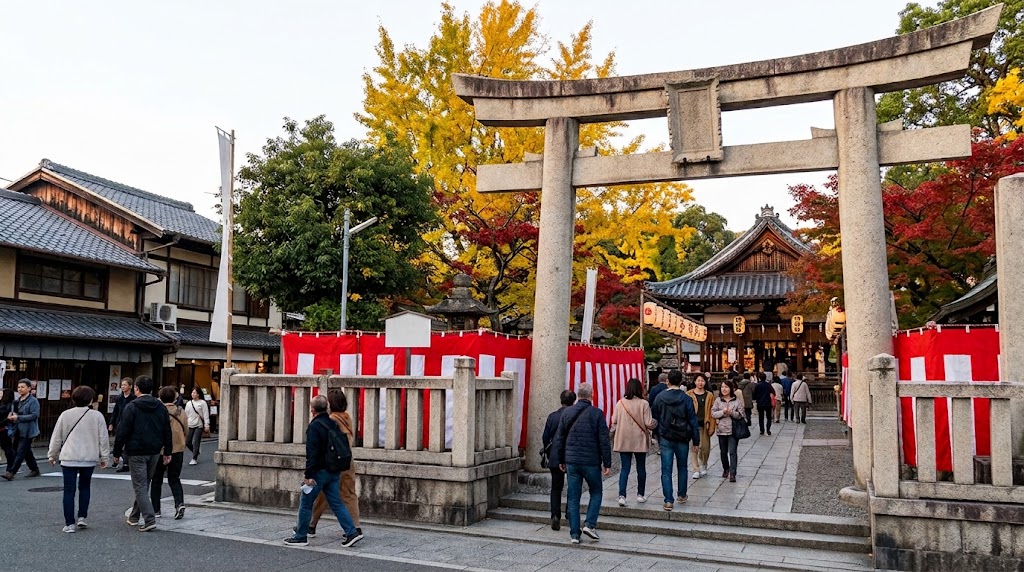 紅葉やイチョウが色づく秋の白峯神宮の入り口で、紅白の幕が張られた巨大な石造りの鳥居をくぐり、伴緒社祭に参拝するため境内へ進む人々